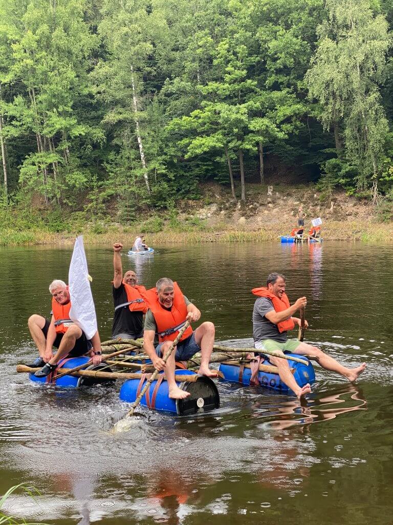 Vier Männer, die auf einem selbstgebauten Floß paddeln auf einem Teich im Wald