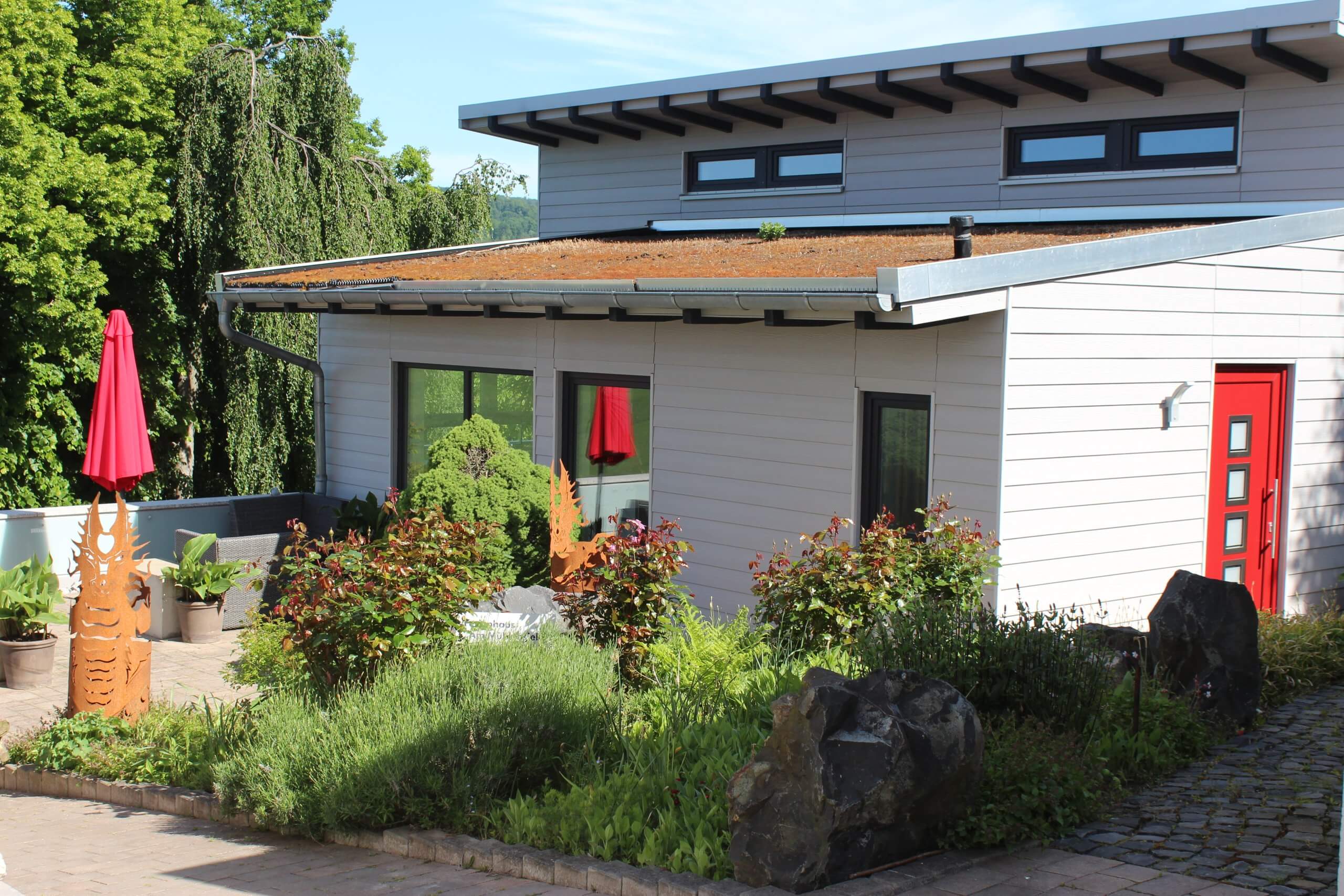 Ein Bungalow mit weißer Holzverkleidung und Vorgarten mit Sonnenschirm